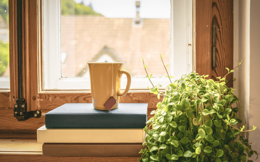 Holzfenster, davor eine Tasse tee und ein kleiner Bücherstapel.